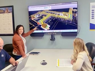 S&B engineers Lindsay Haines points to engineering schematics on a large TV in a conference room with fellow engineer Sophie Dupree.