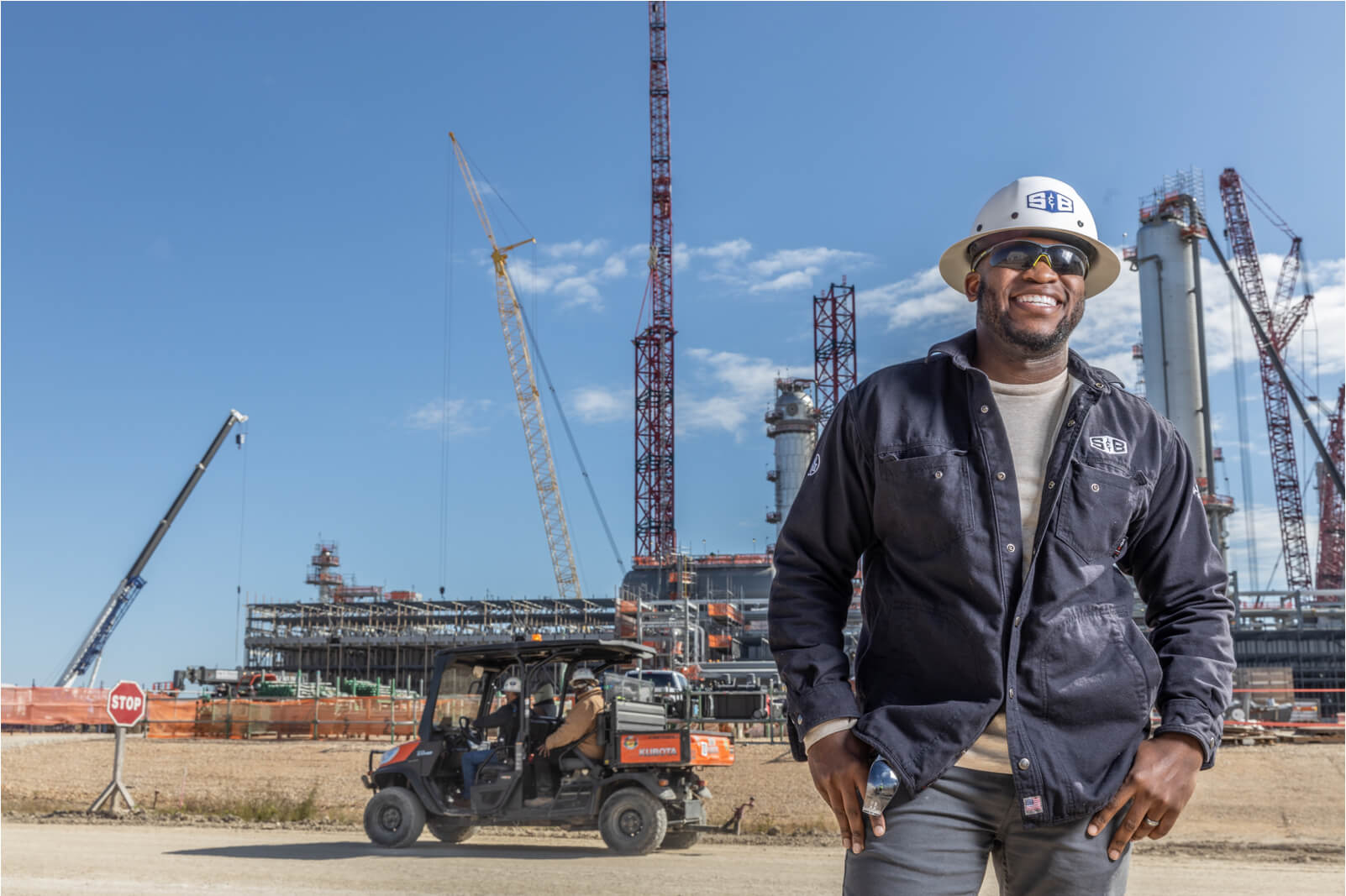 S&B Employee wearing a hard hat in front of a refinery