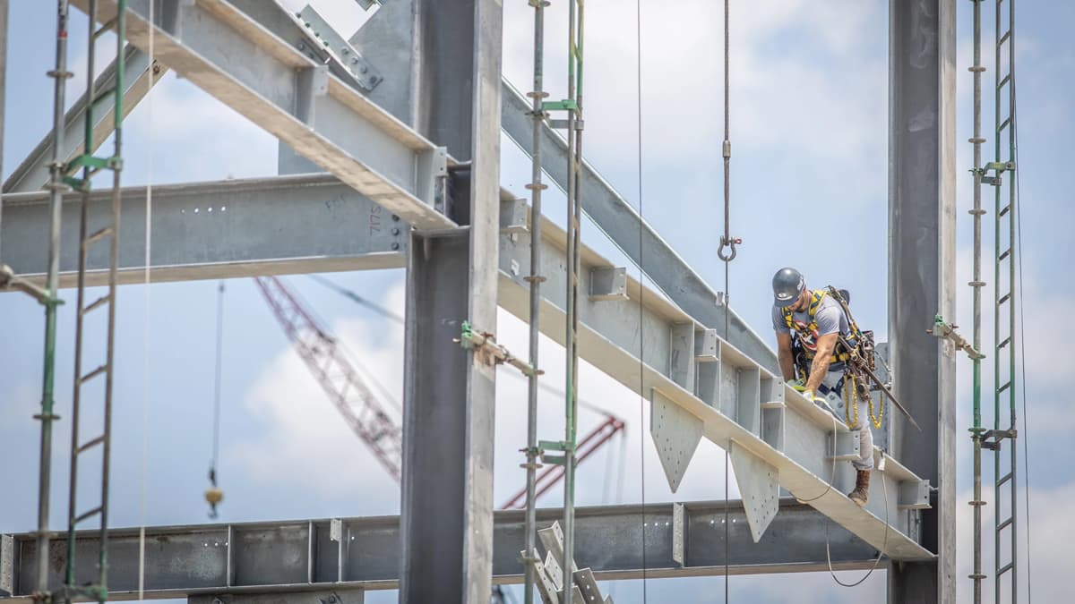 A S&B construction worker climbing on a steel girder with tools