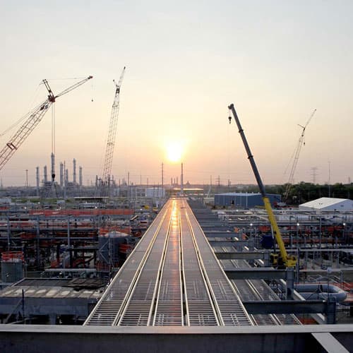 A large facility under construction with cranes all around and with the sun setting int he background